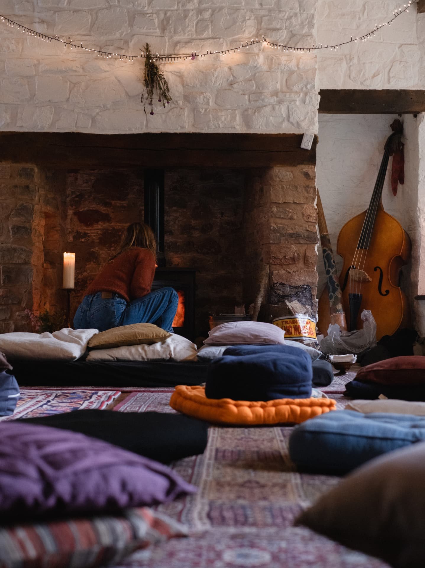 Candlelit gathering room with floor cushions around a stone fireplace